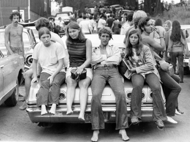 six kids sitting on the back of sedan with only one of them wearing shoes.